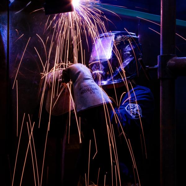 VIU student practices their welding techniques. Sparks are flying and their helmet is reflecting purple light.