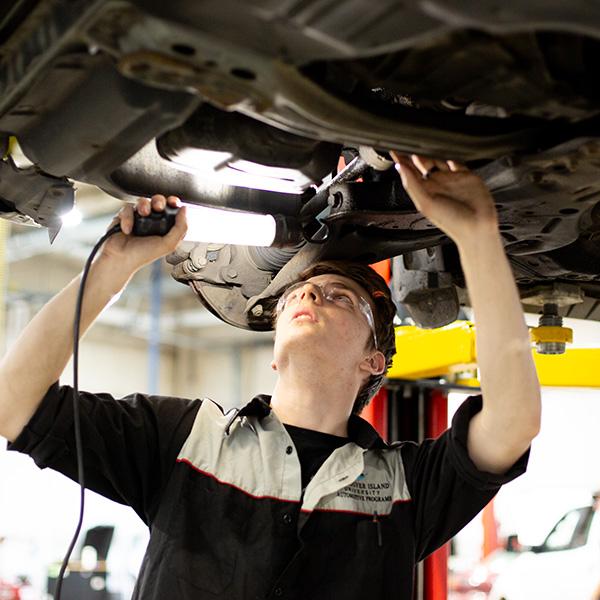 A man using a light to inspect the under carriage of a car.  