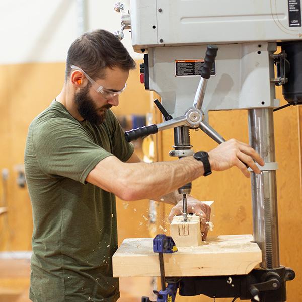 A man using a drill press in a workshop. 