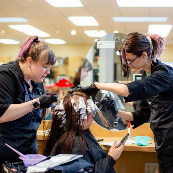 two hairdressing students apply colour to a customers hair