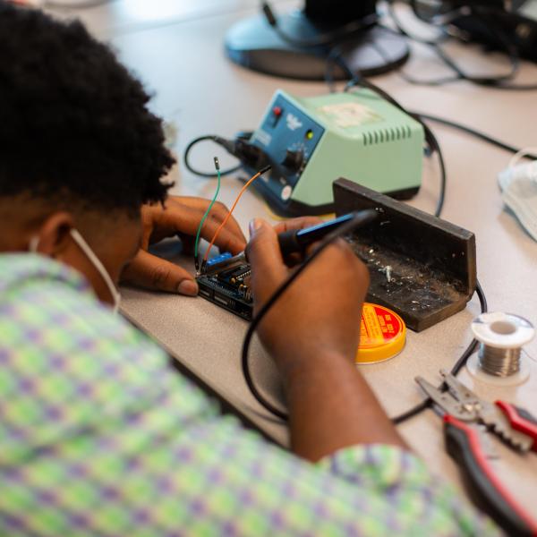 We are looking over the shoulder of a VIU ITAS student while they solder part of their final project.