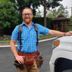 Smiling man wearing a checked shirt and tool belt.