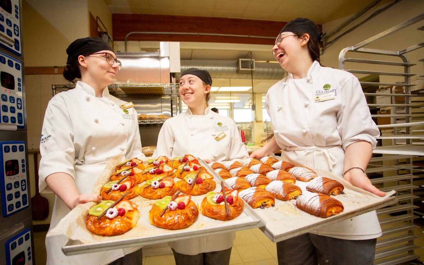 three baking students laughing and holding a sheet of baked goods 